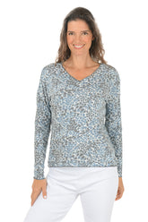 Woman wearing a patterned long-sleeve top and white pants on a white background.