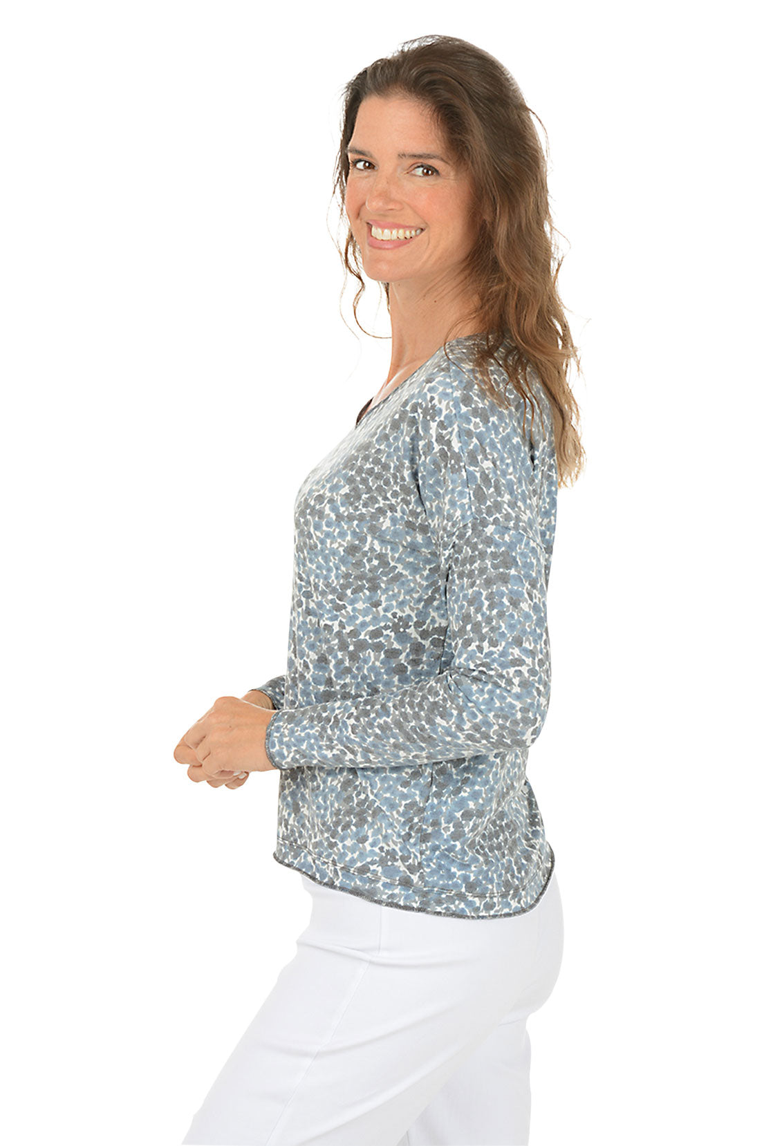 Woman wearing a patterned long-sleeve top and white pants on a white background. Side shot.