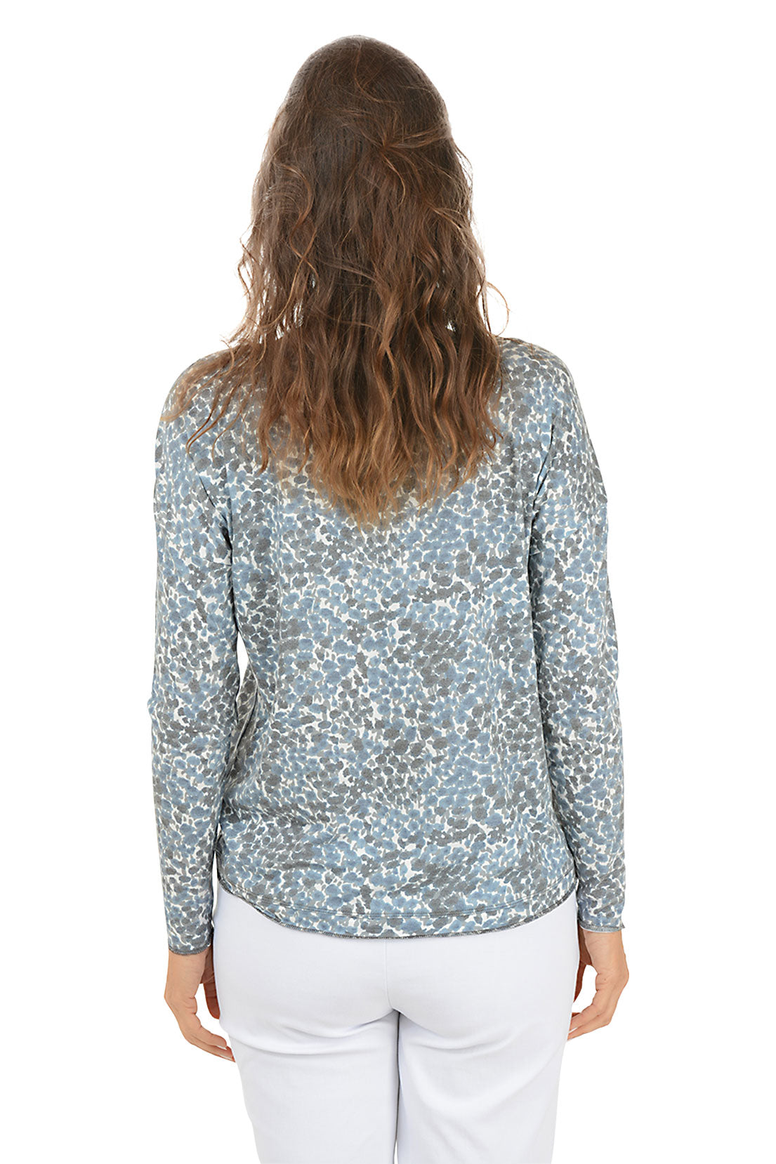 Woman wearing a patterned long-sleeve top and white pants on a white background. Back shot.