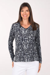 A woman wearing a navy and white botanical print V-neck sweater with long sleeves and white pants.
