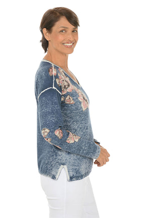 Woman wearing a blue floral-patterned sweater on a white background. Side shot.