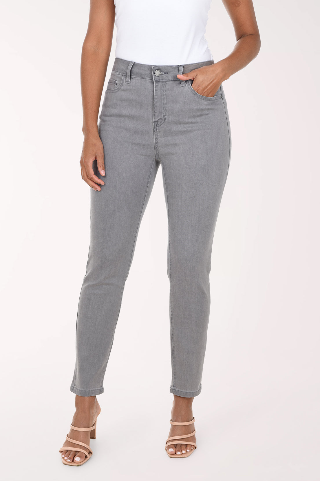 A model wearing a pair of light gray slim-fit jeans with a white top and beige heeled sandals, shown from the waist down against a plain white studio background.
