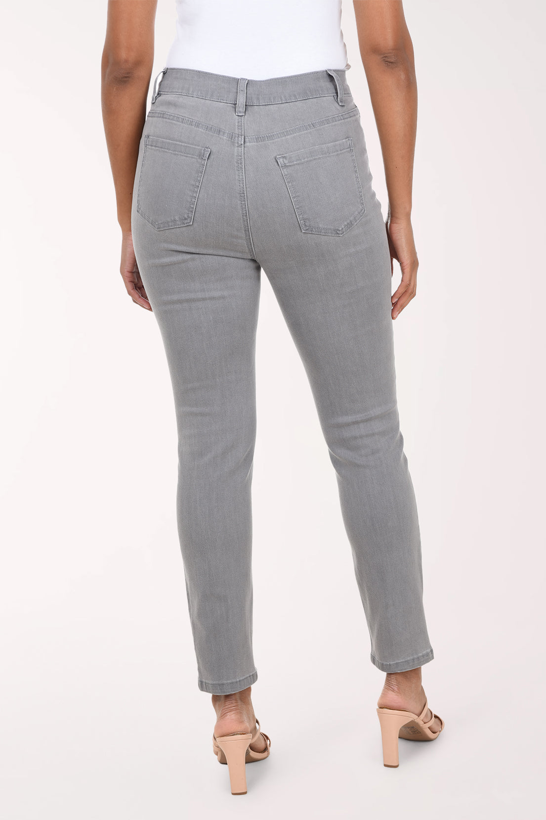 A model wearing a pair of light gray slim-fit jeans with a white top and beige heeled sandals, shown from the waist down against a plain white studio background.