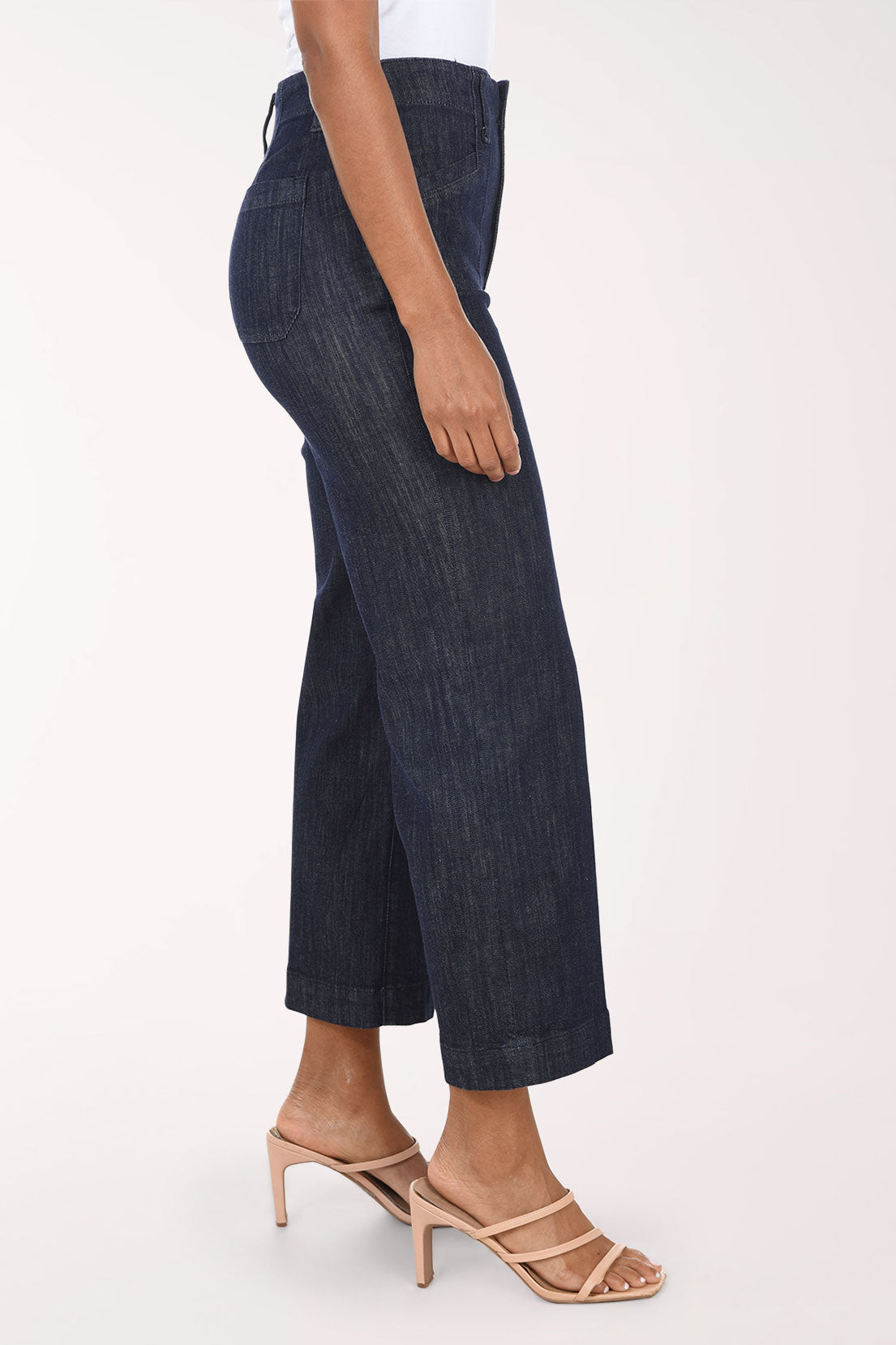 A model wearing dark wash cropped wide-leg denim jeans with a white top and beige heeled sandals, shown from the waist down against a plain white studio background.