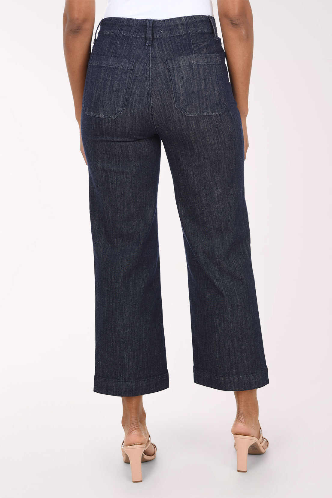 A model wearing dark wash cropped wide-leg denim jeans with a white top and beige heeled sandals, shown from the waist down against a plain white studio background.