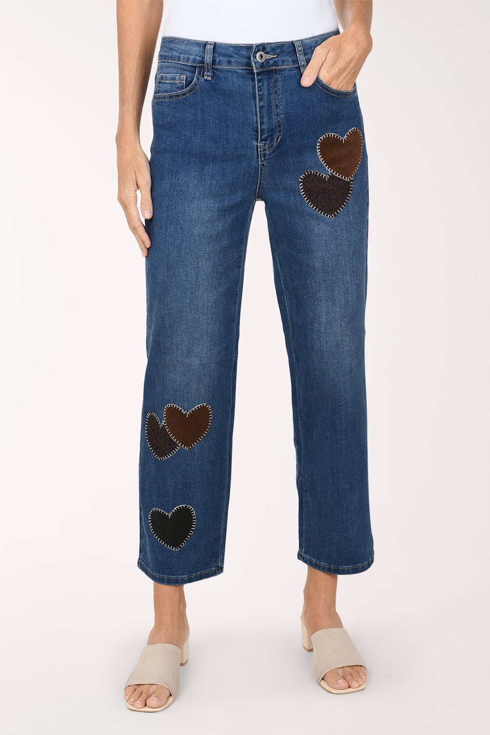 A front view of medium wash straight leg jeans with dark brown and black heart-shaped patches on the legs, worn with nude sandals.