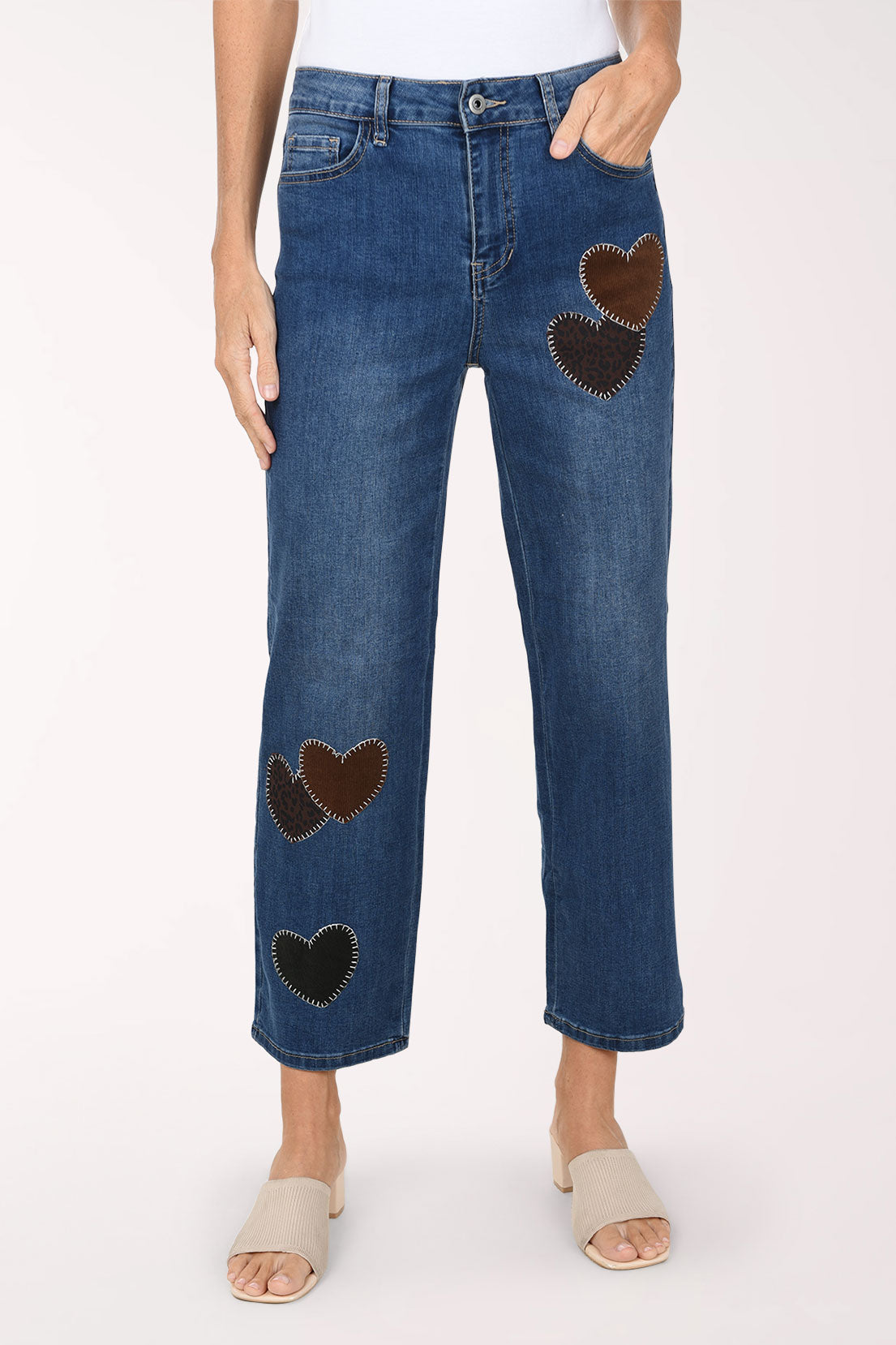 A front view of medium wash straight leg jeans with dark brown and black heart-shaped patches on the legs, worn with nude sandals.
