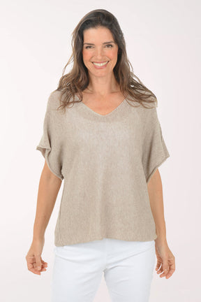 Woman wearing a beige top and white pants on a white background