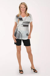 Woman wearing a white tunic with abstract black and gray design and black shorts on a white background
