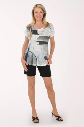 Woman wearing a white tunic with abstract black and gray design and black shorts on a white background