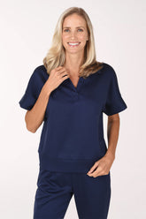 Front view of a woman in a navy Jet Blue scuba knit polo top with an open V-neckline and collar, short cuffed dolman sleeves and a straight hem, worn with matching navy pants.