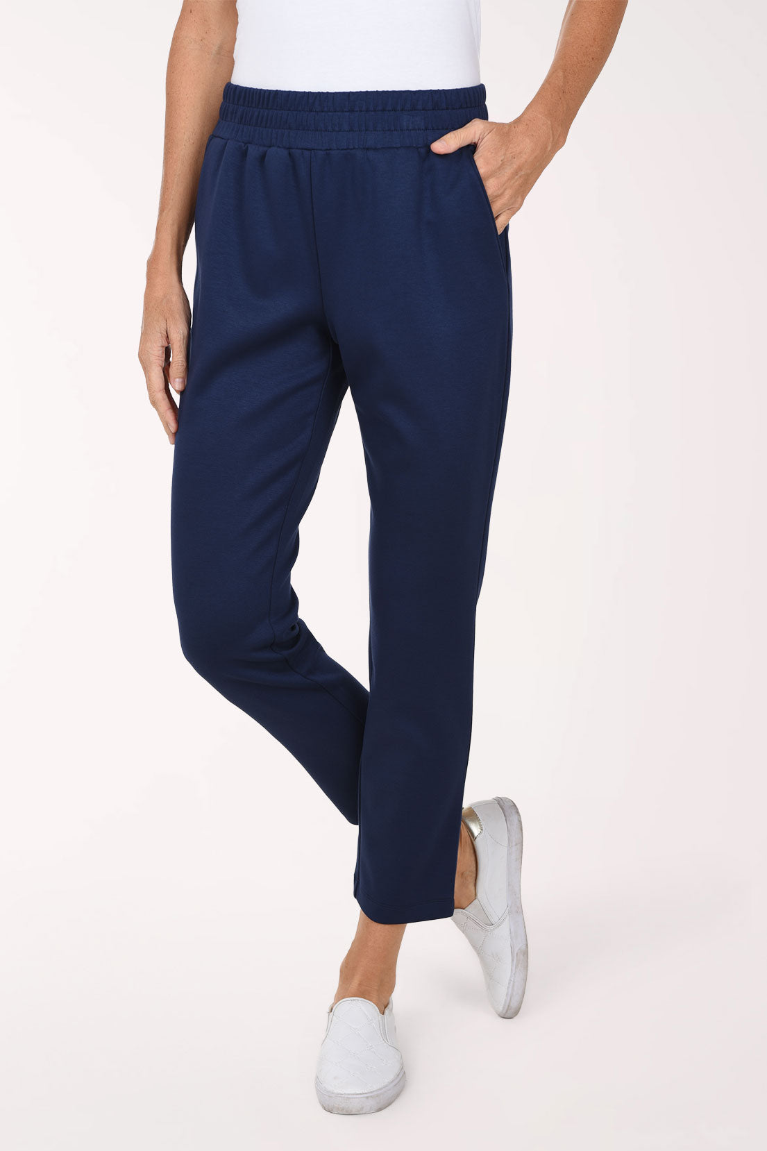 Front view of navy Jet Blue scuba straight leg pants with a smocked stretch waistband and front pocket, shown with one hand in the pocket and white sneakers.