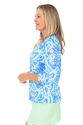A woman wearing a blue heart patterned v-neck top with 3/4 sleeves. Side shot.