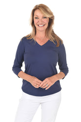 Woman wearing a navy blue 3/4 sleeve v-neck top and white pants on a white background.