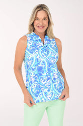 Woman wearing a blue patterned sleeveless top and light green pants on a white background