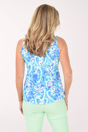Woman wearing a blue patterned sleeveless top and light green pants on a white background