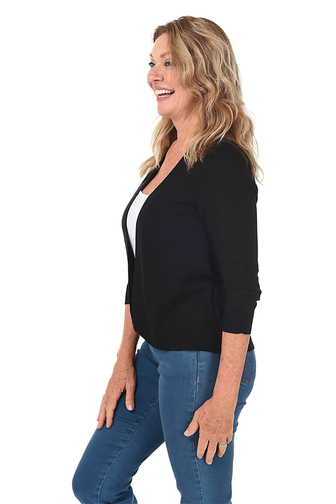 Side shot of a woman wearing a black cardigan over a white top and blue jeans on a white background