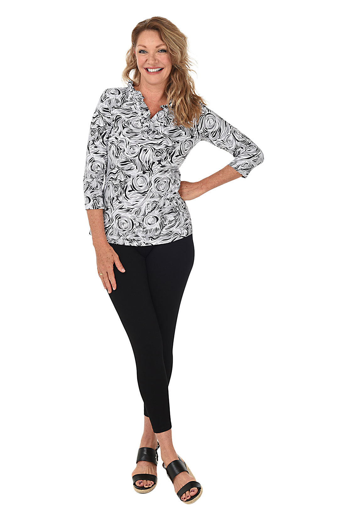 A woman wearing black ankle length leggings with a rhinestone-accented zipper on the back hemline. Full length shot.