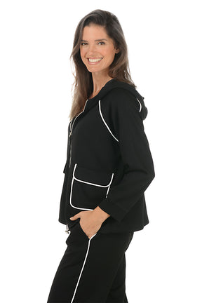 Woman wearing a black hoodie with white accents on a white background. Side shot.