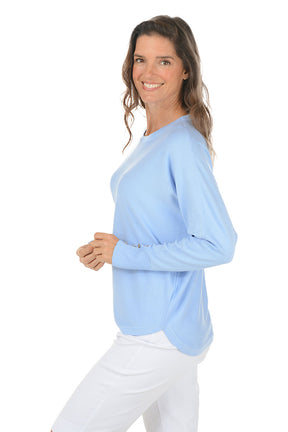 Woman wearing a light blue sweater and white pants on a white background. Side shot.