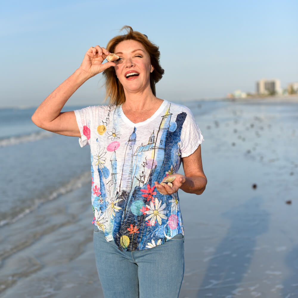 Woman on a beach holding seashells with a clear blue sky in the background