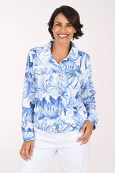 A woman wearing a blue and white tropical floral print button-up jacket and white pants, standing against a plain light background.