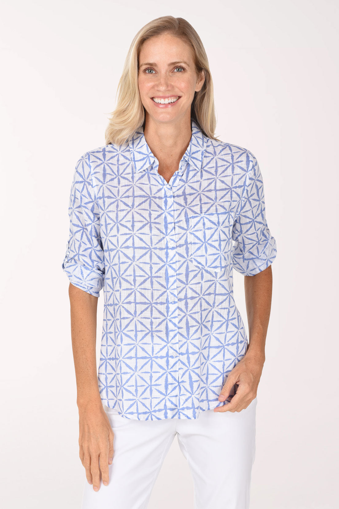 A smiling blonde woman wearing a light blue and white geometric patterned button-down shirt, posing against a solid off-white studio background.