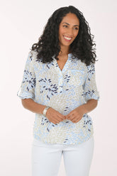 Woman wearing a patterned blouse and white pants on a plain background