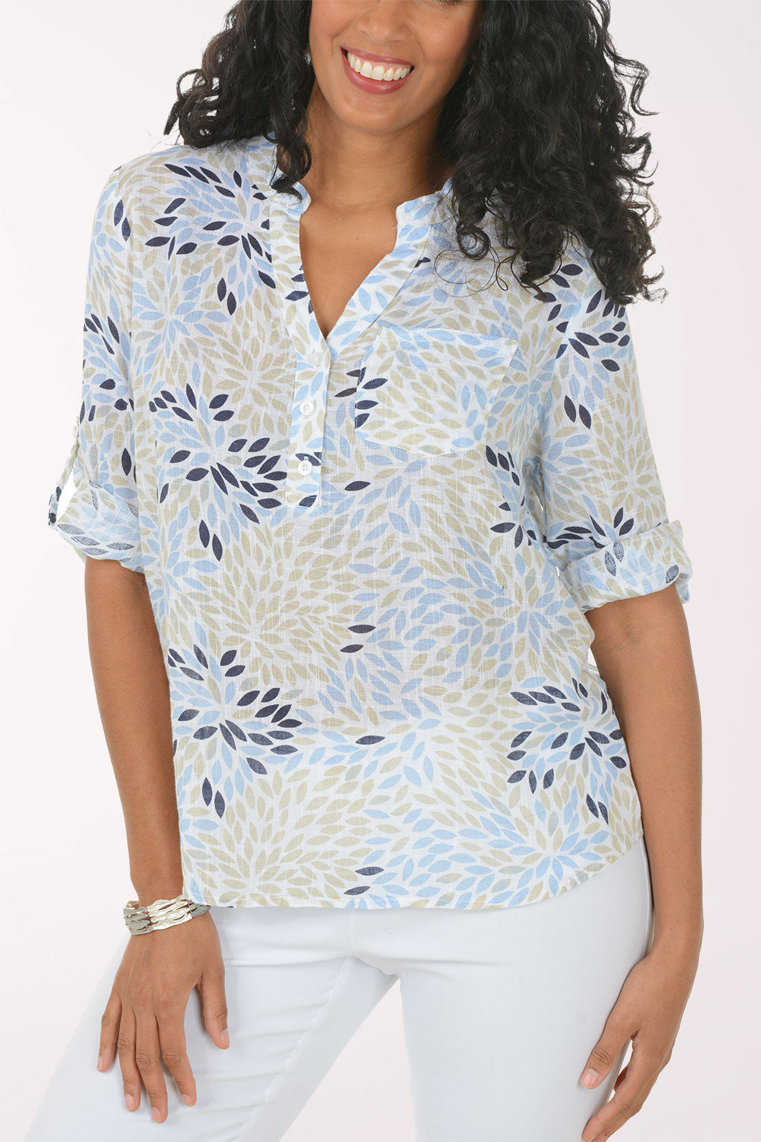Woman wearing a patterned blouse and white pants on a plain background