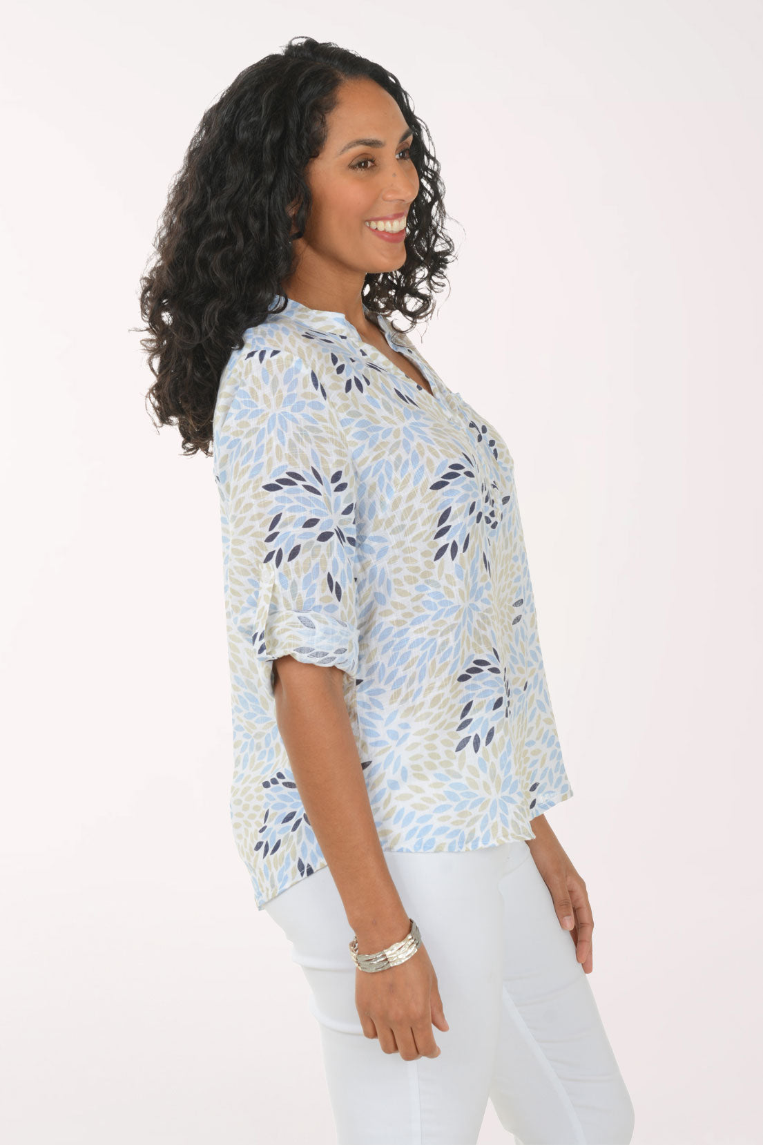 Woman wearing a patterned blouse and white pants on a plain background