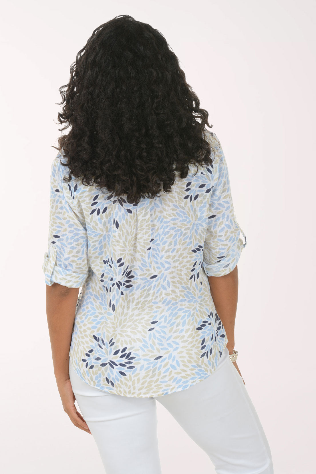 Woman wearing a patterned blouse and white pants on a plain background