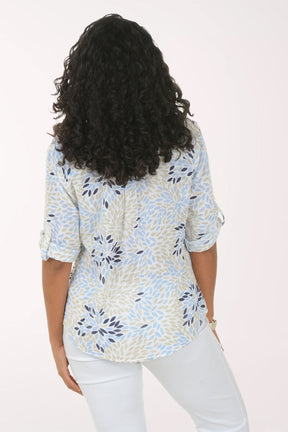 Woman wearing a patterned blouse and white pants on a plain background