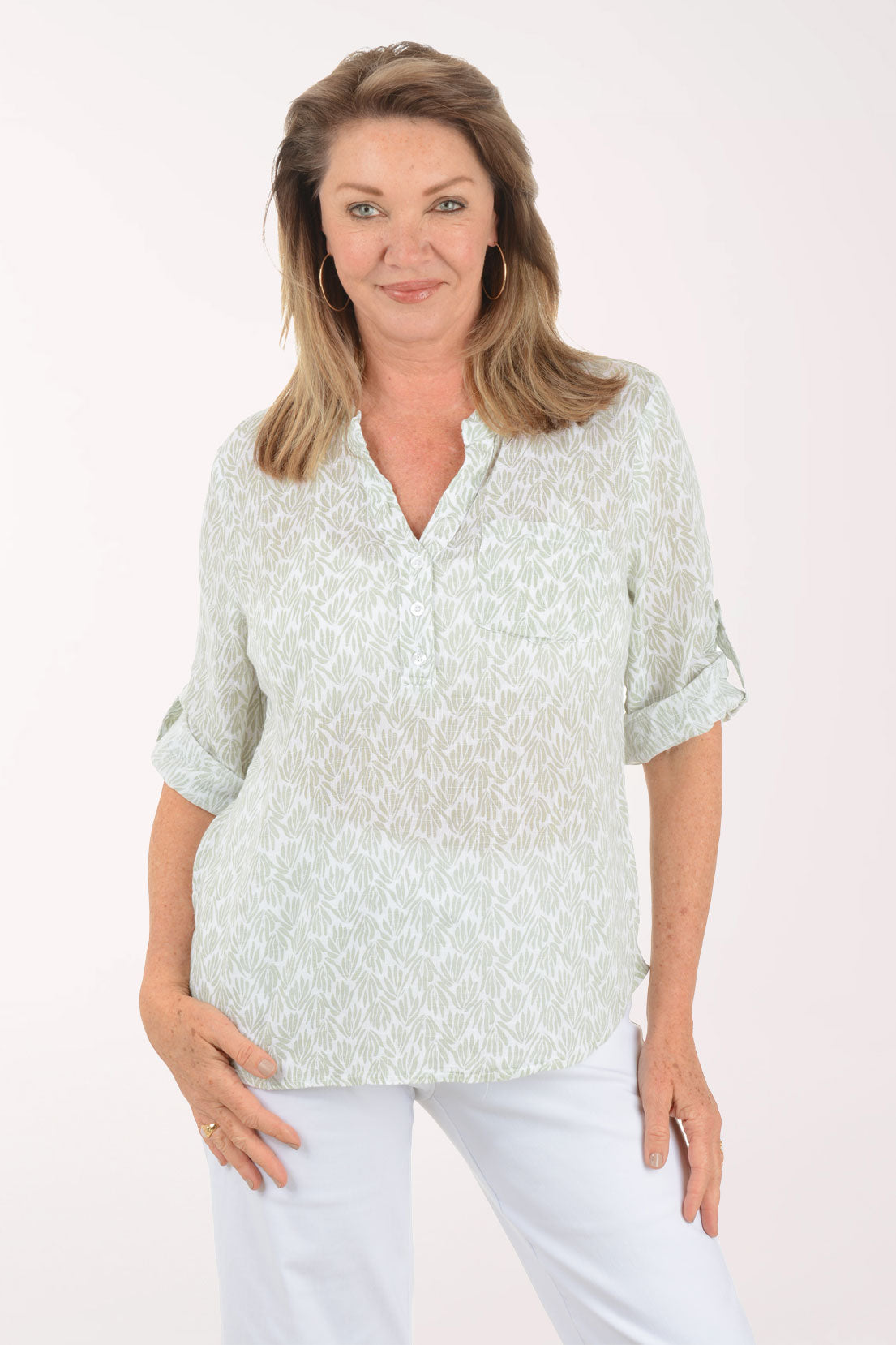 Woman wearing a light green patterned blouse and white pants on a white background