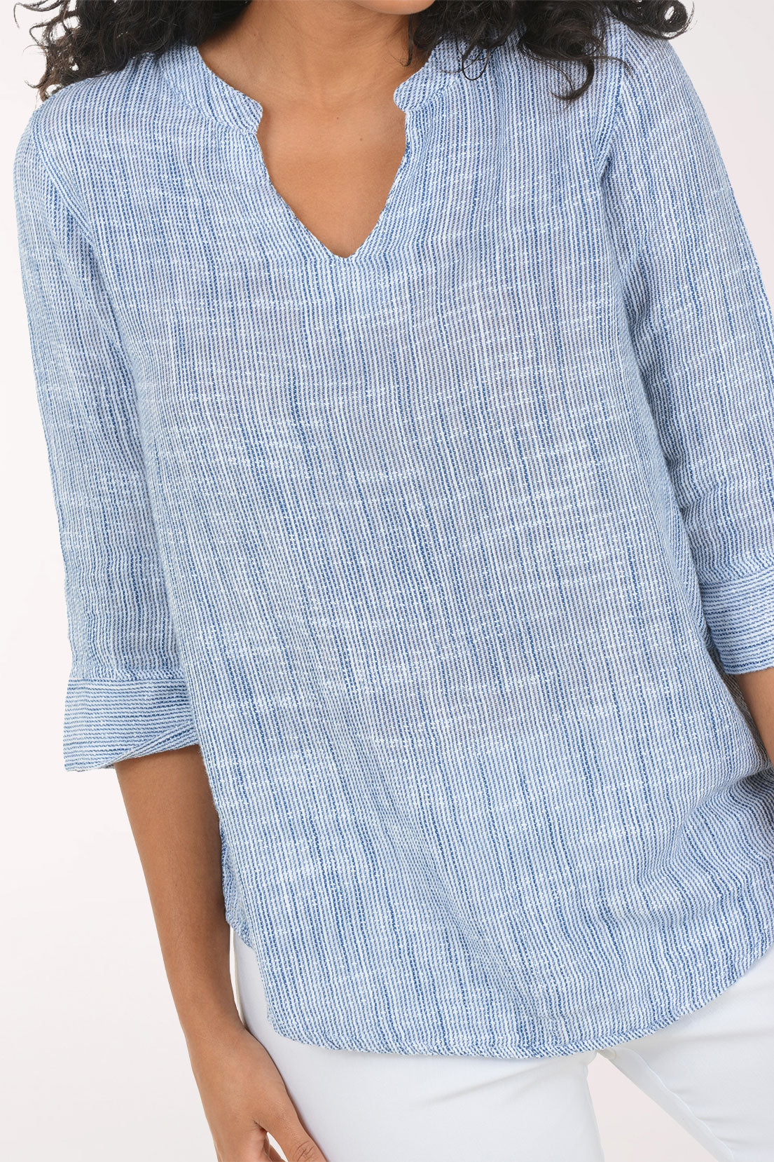 Woman wearing a blue checkered blouse and white pants on a white background