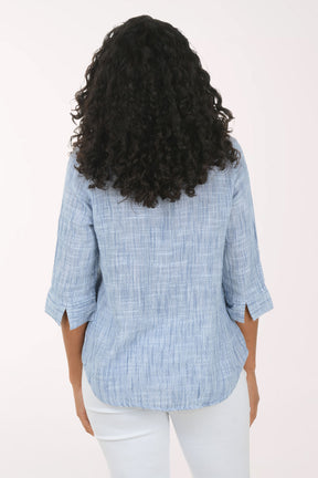 Woman wearing a blue checkered blouse and white pants on a white background