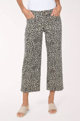 A person wearing cropped wide-leg pants with an olive green, black, and beige animal print, paired with a white top and beige slide sandals, against a plain white studio background.