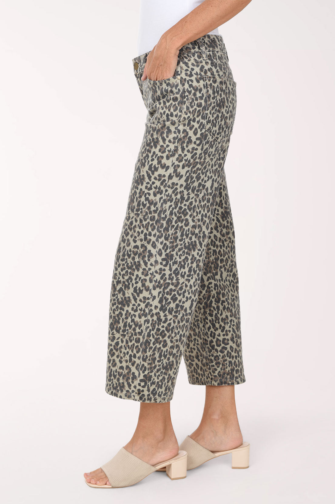 A person wearing cropped wide-leg pants with an olive green, black, and beige animal print, paired with a white top and beige slide sandals, against a plain white studio background.