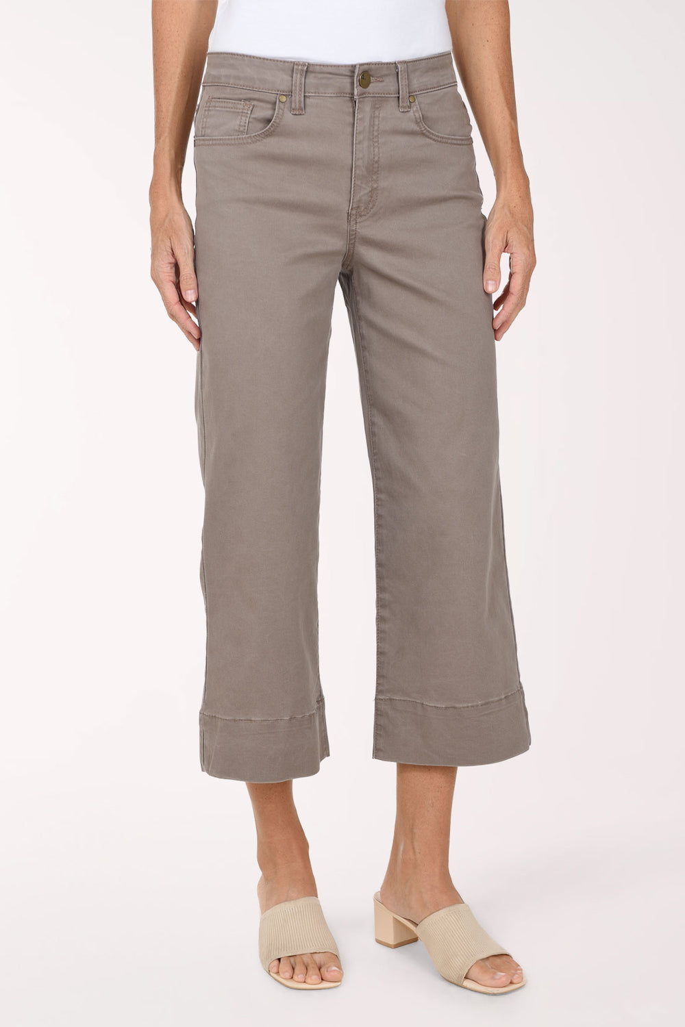 A model wearing a pair of taupe cropped wide-leg jeans with rolled hems, paired with beige slide sandals, against a plain light background.