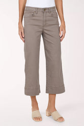 A model wearing a pair of taupe cropped wide-leg jeans with rolled hems, paired with beige slide sandals, against a plain light background.