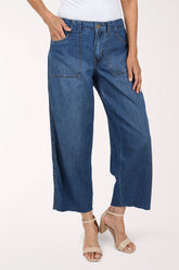 A model wearing a pair of wide-leg cropped blue denim jeans with a white top and beige heeled sandals, shown from the waist down against a plain white studio background.