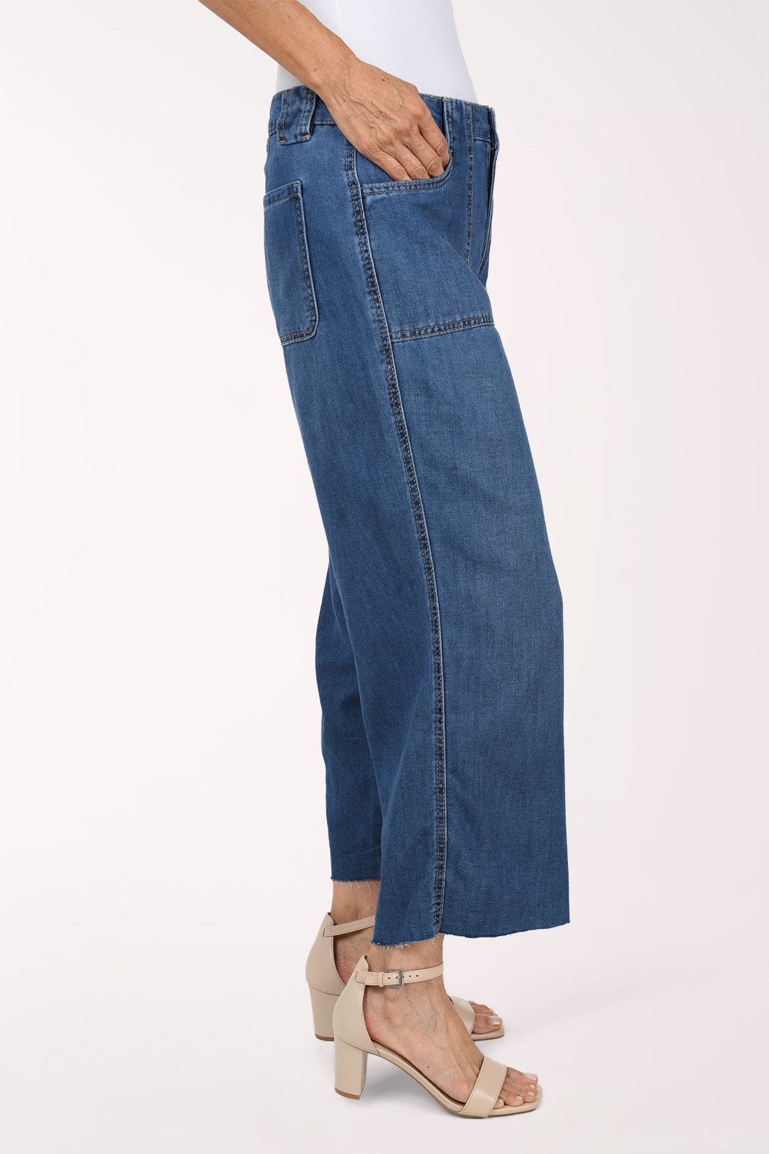 A model wearing a pair of wide-leg cropped blue denim jeans with a white top and beige heeled sandals, shown from the waist down against a plain white studio background.