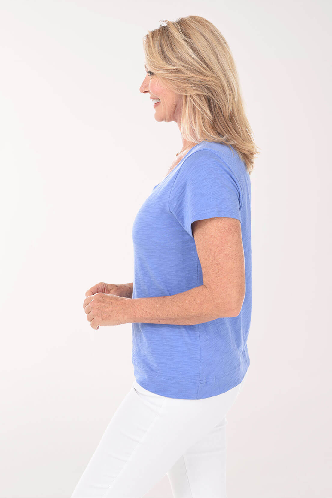 Woman wearing a blue t-shirt and white pants on a white background. Side shot.