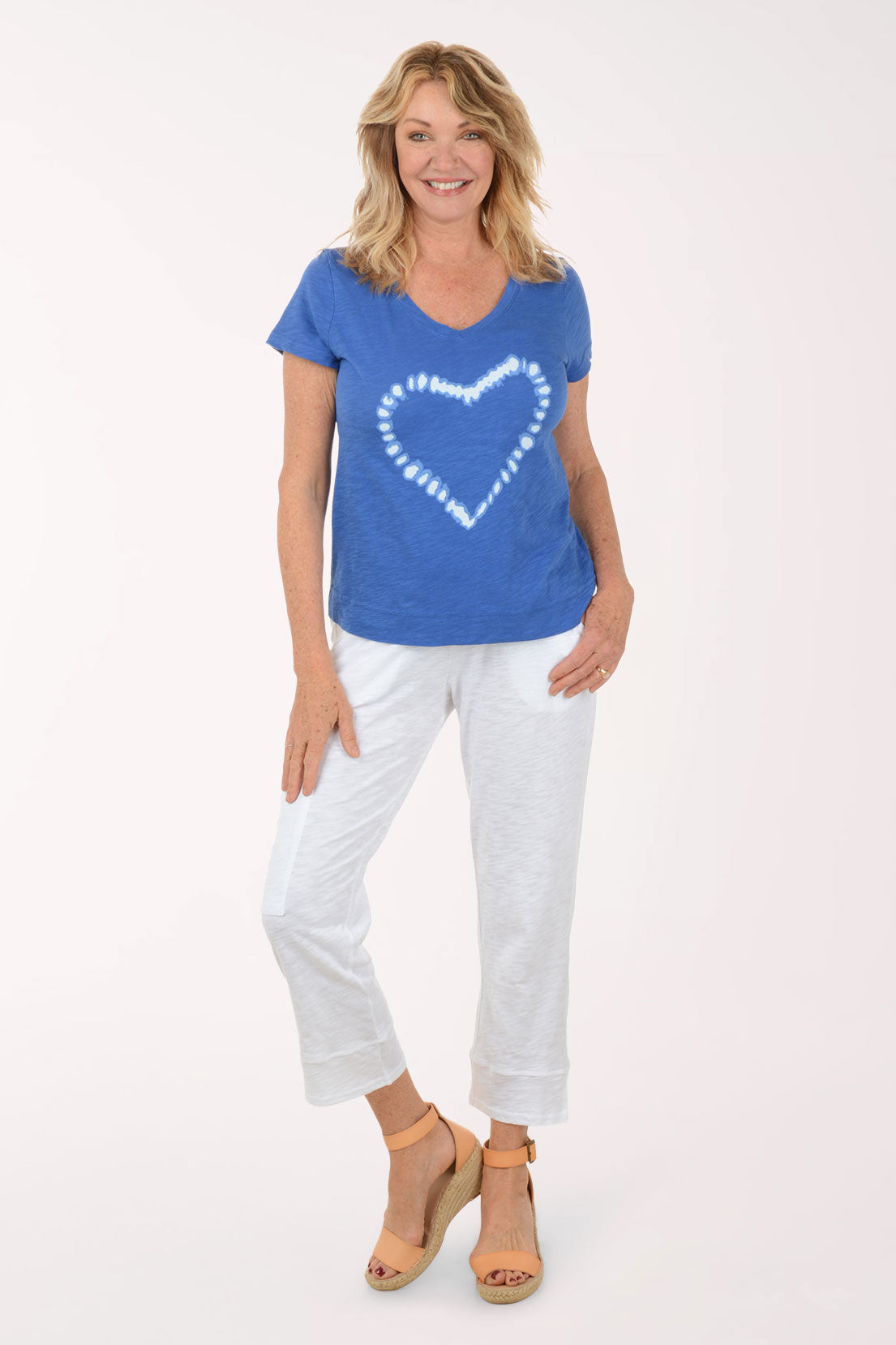 Woman wearing a blue t-shirt with a white heart design and white pants on a white background