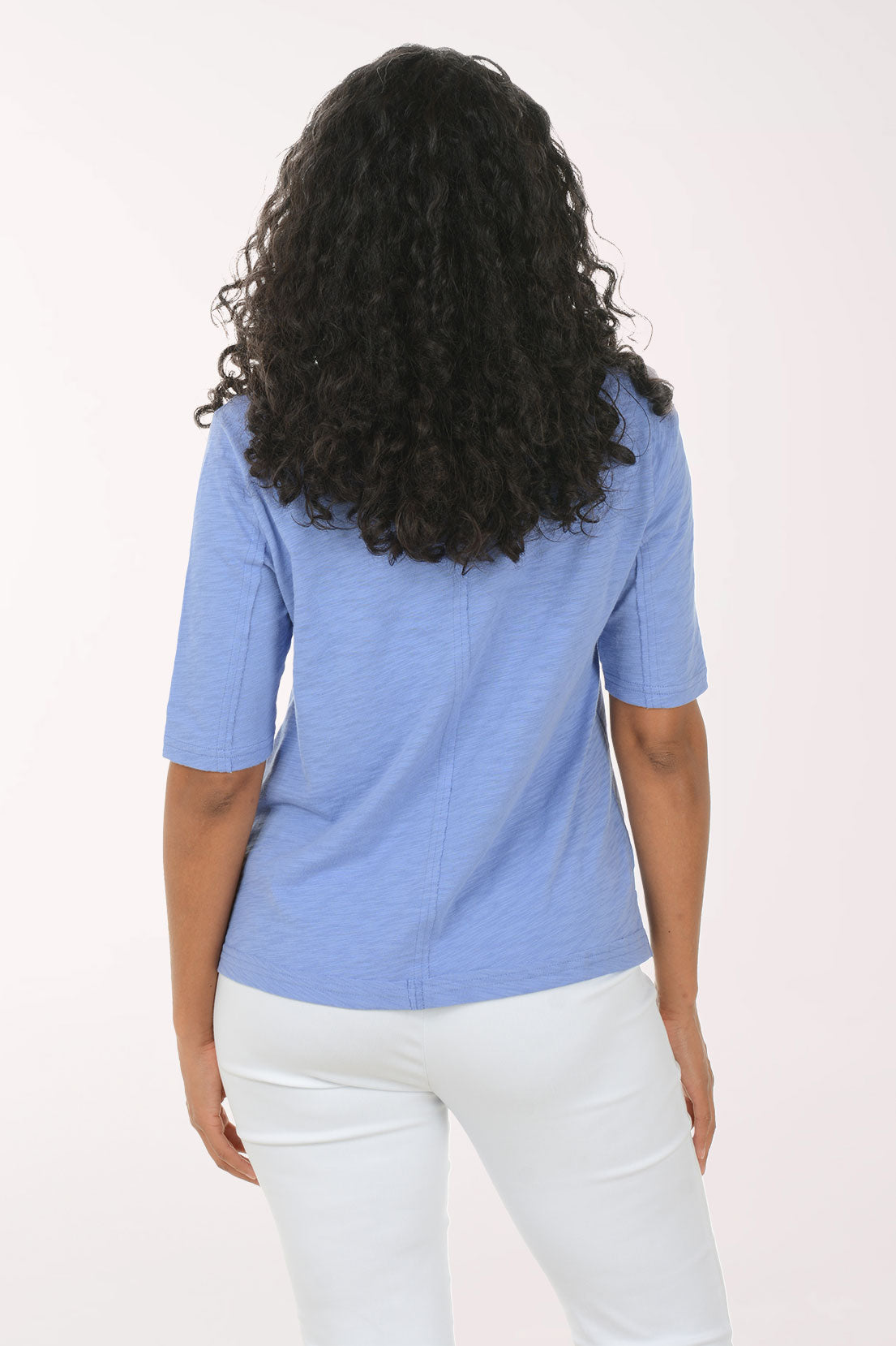 Person wearing a blue top and white pants on a light pink background