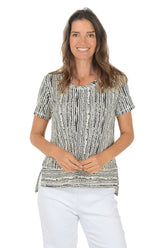 Woman wearing a patterned top and white pants on a white background.