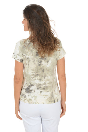 Woman wearing a patterned top and white pants on a white background. Back shot.