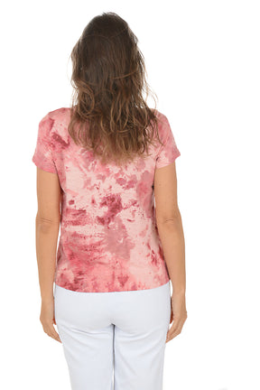 Woman wearing a pink floral top and white pants on a white background. Back shot.