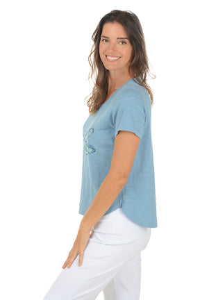 Woman wearing a blue t-shirt with a dragonfly design on a white background. Side shot.