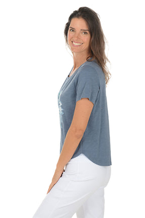 Woman wearing a blue t-shirt with a floral design on a white background. Side shot.