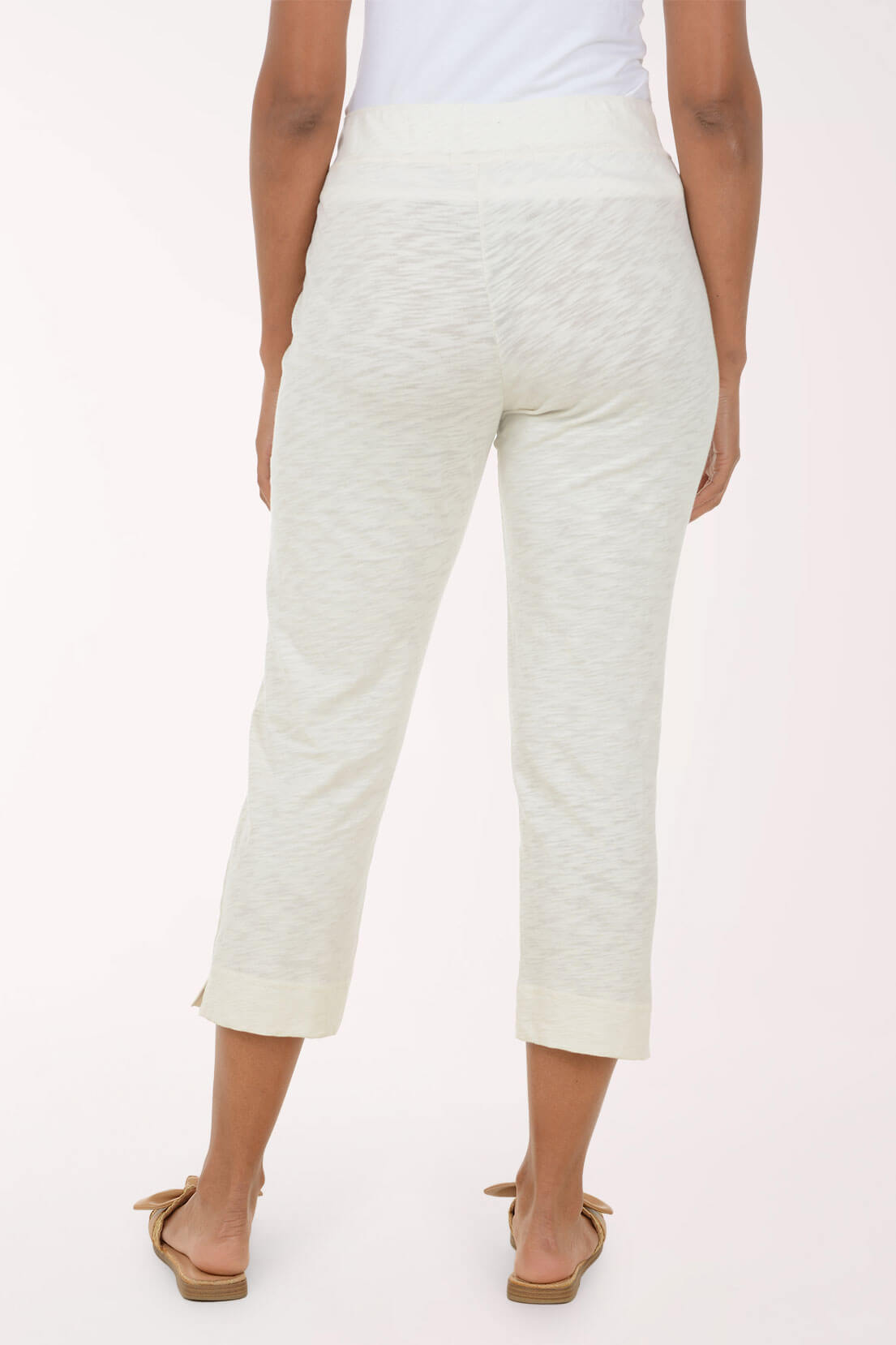 A model shown from the back wearing high-waisted, cropped, heathered off-white pants and tan flat sandals against a plain light background.
